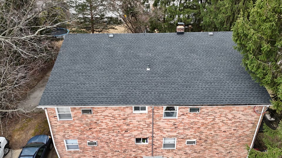 A finished grey shingle roof on a brick house