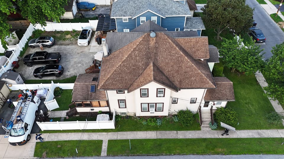 Drone view of a two story house with a worn brown shingle roof, before the reroof