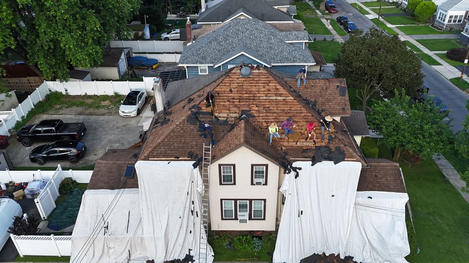 Drone view of the same house with the old shingles coming off and tarps laid around the yard