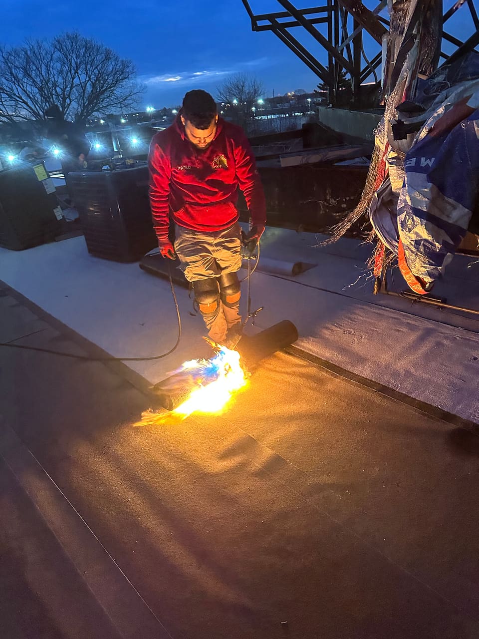 A roofer torching down membrane at dusk
