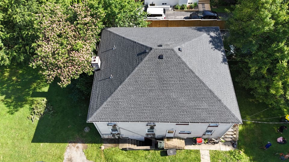 The finished hip roof in grey shingles, straight down from the drone