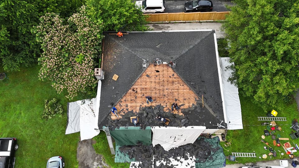 Drone view of a hip roof part way through a tear off, old shingles on tarps below