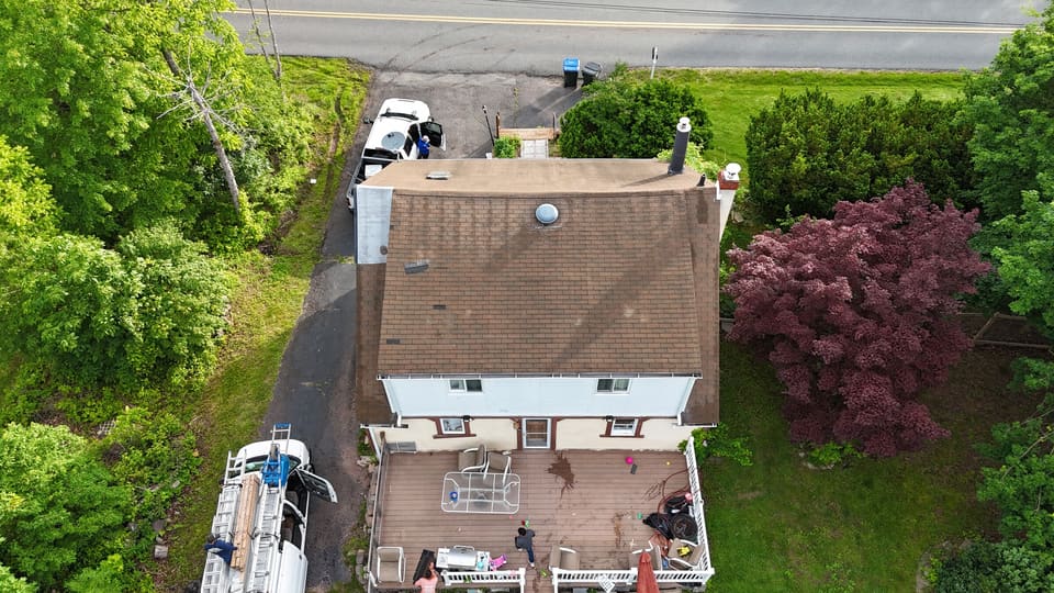 Drone view of a house with a tired brown roof next to a red maple, before work started