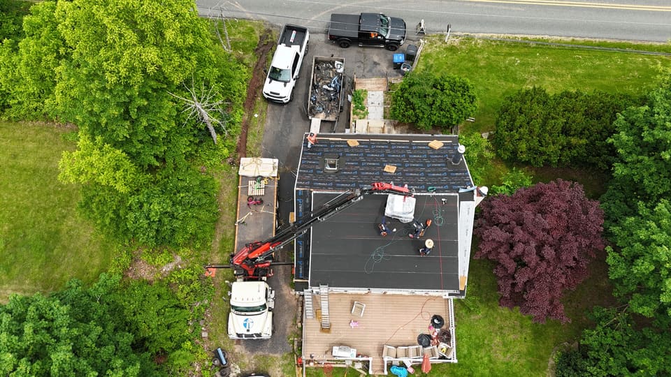 New roofing going down while a crane lifts material over the house