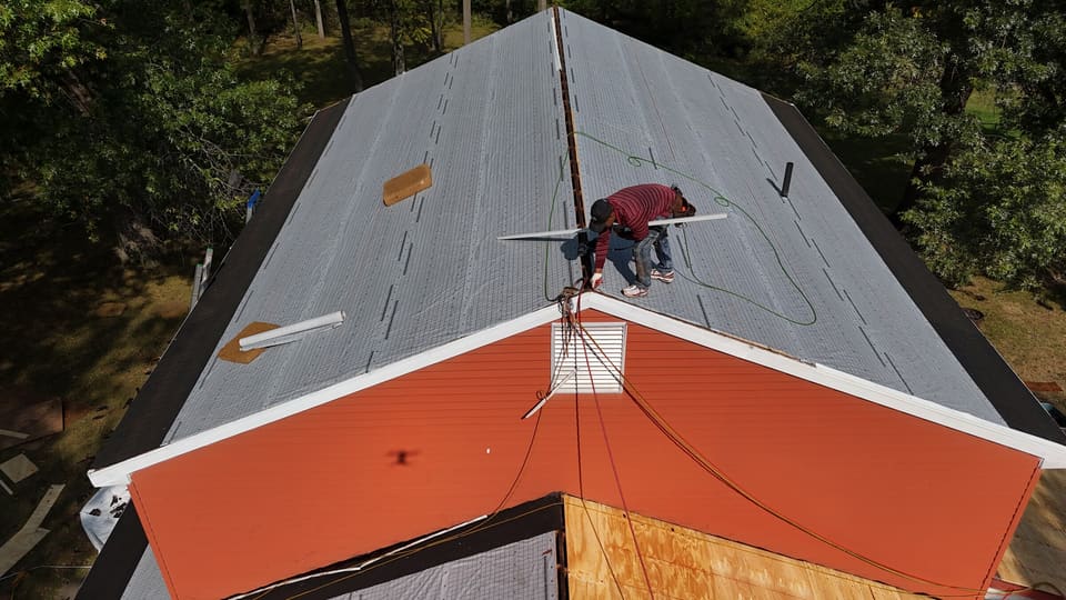 A roofer at the ridge of the underlayment above the orange siding