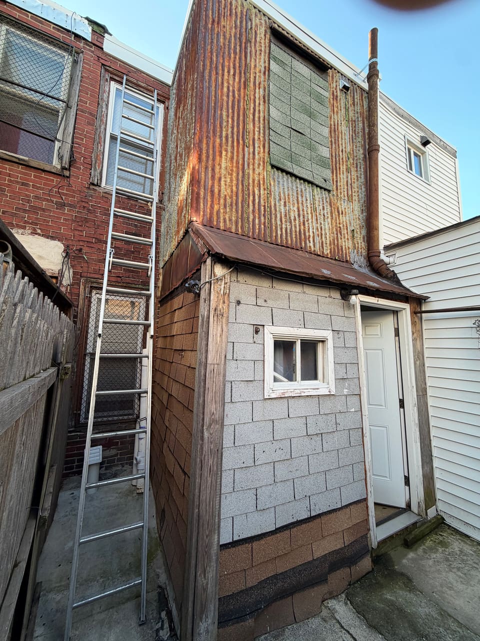 A row home rear with worn wood and shingle siding, before