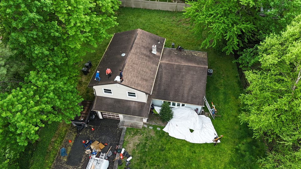 Drone view of a split level house with a worn brown roof and tarps on the lawn