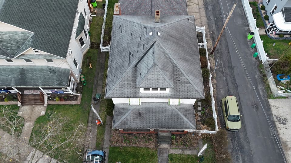 Drone view of a house before its reroof, street and parked cars below