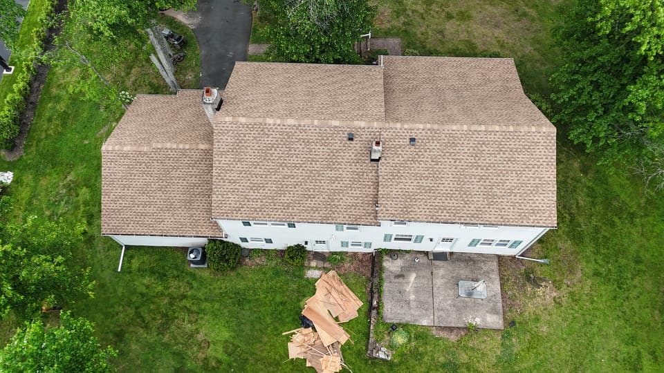 A finished tan shingle roof with shingle wrappers in the yard